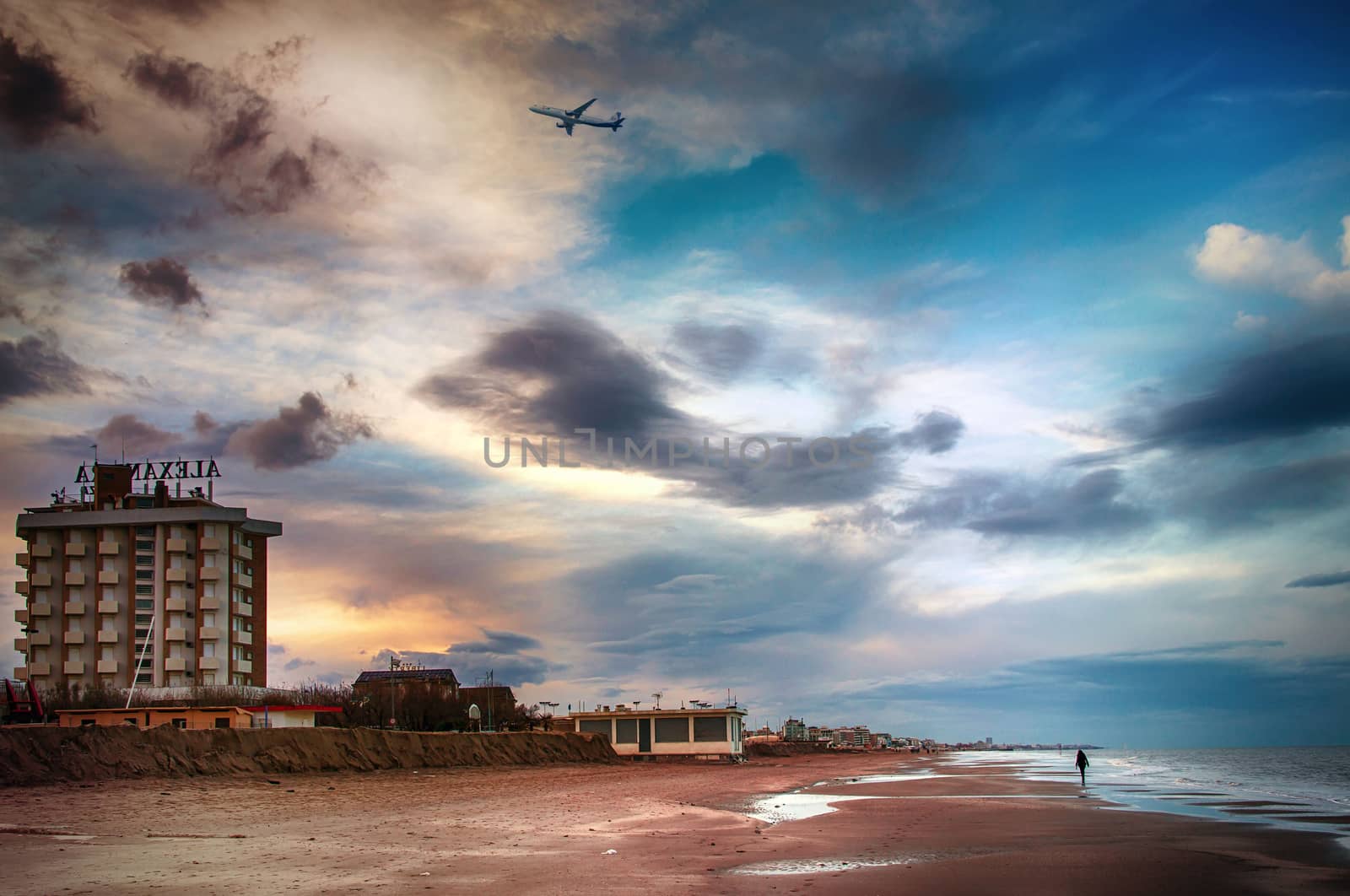 a woman is walking alone on the seashore and a plane is passing by over her head