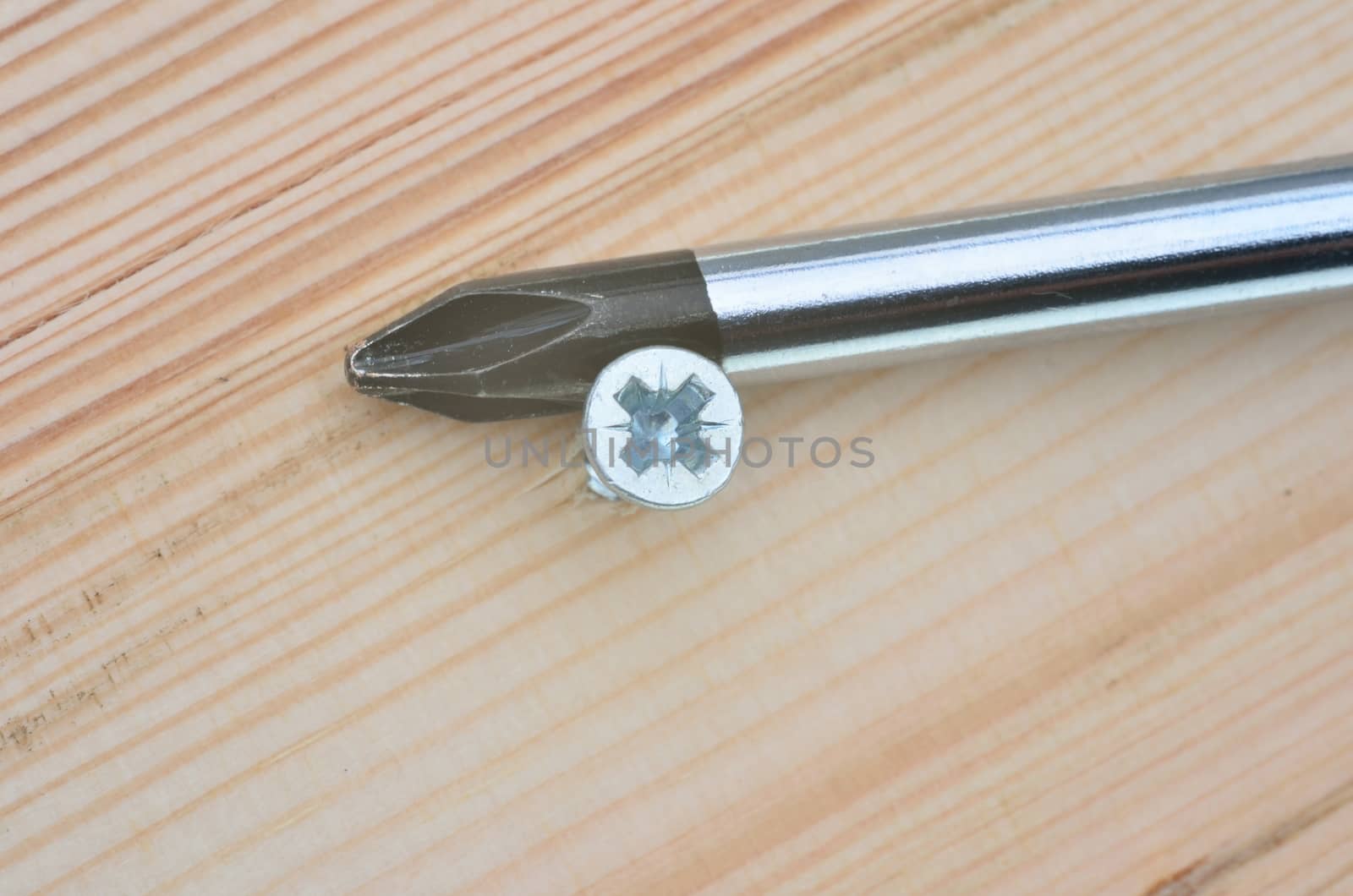 Screwdriver and screw in close up with wooden background