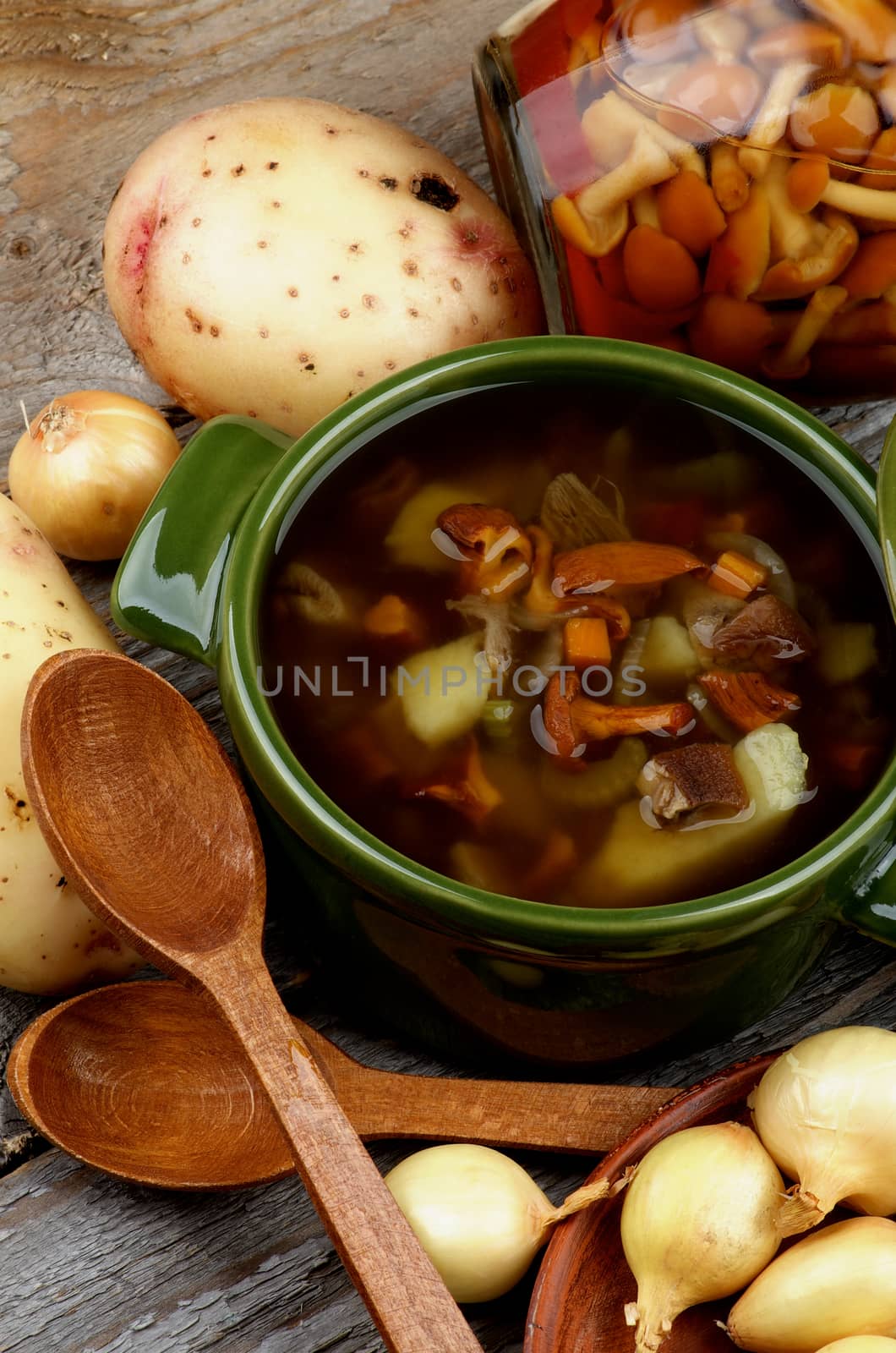 Delicious Vegetarian Soup with Chanterelle Mushrooms  in Green Pot and Raw Ingredients with Wooden Spoons on closeup Rustic Wooden background