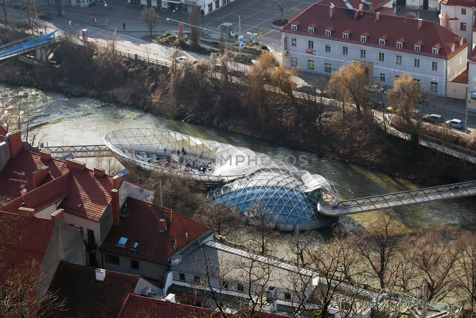 Graz, Austria - January 16, 2011: Island on Mur river connected by a modern steel and glass bridge, Styria, Graz, Austria