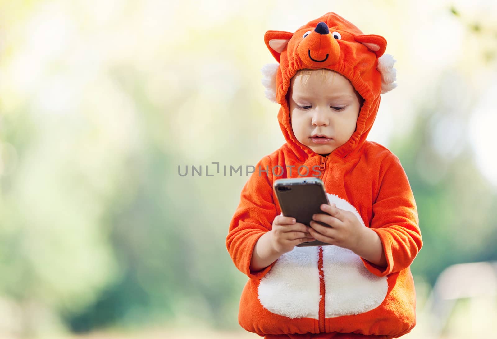 Joyful toddler boy in fox costume holding smartphone