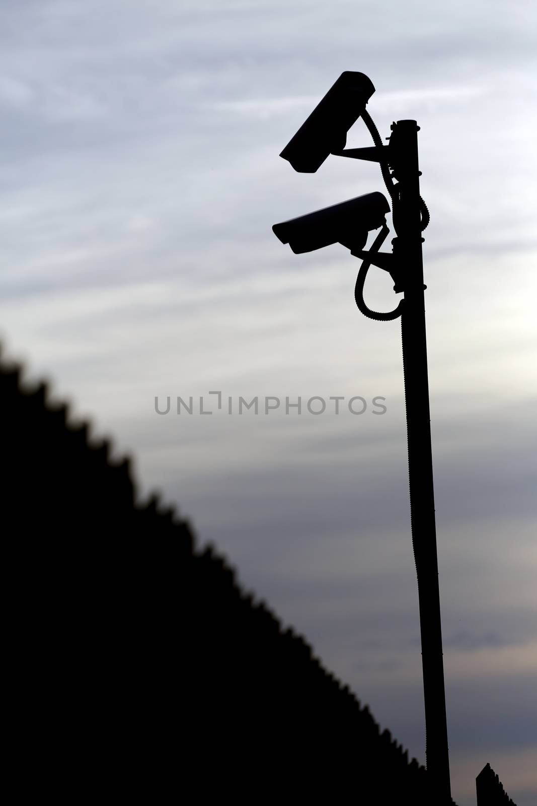 silhouette of two surveillance cameras and a fence