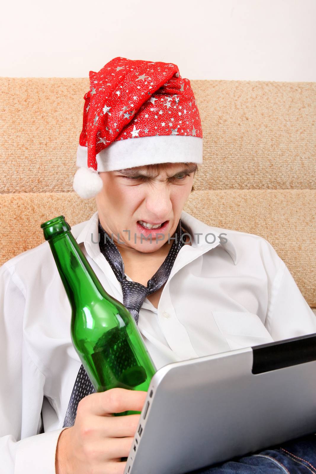 Angry Teenager in Santa Hat with Tablet Computer and Bottle of the Beer