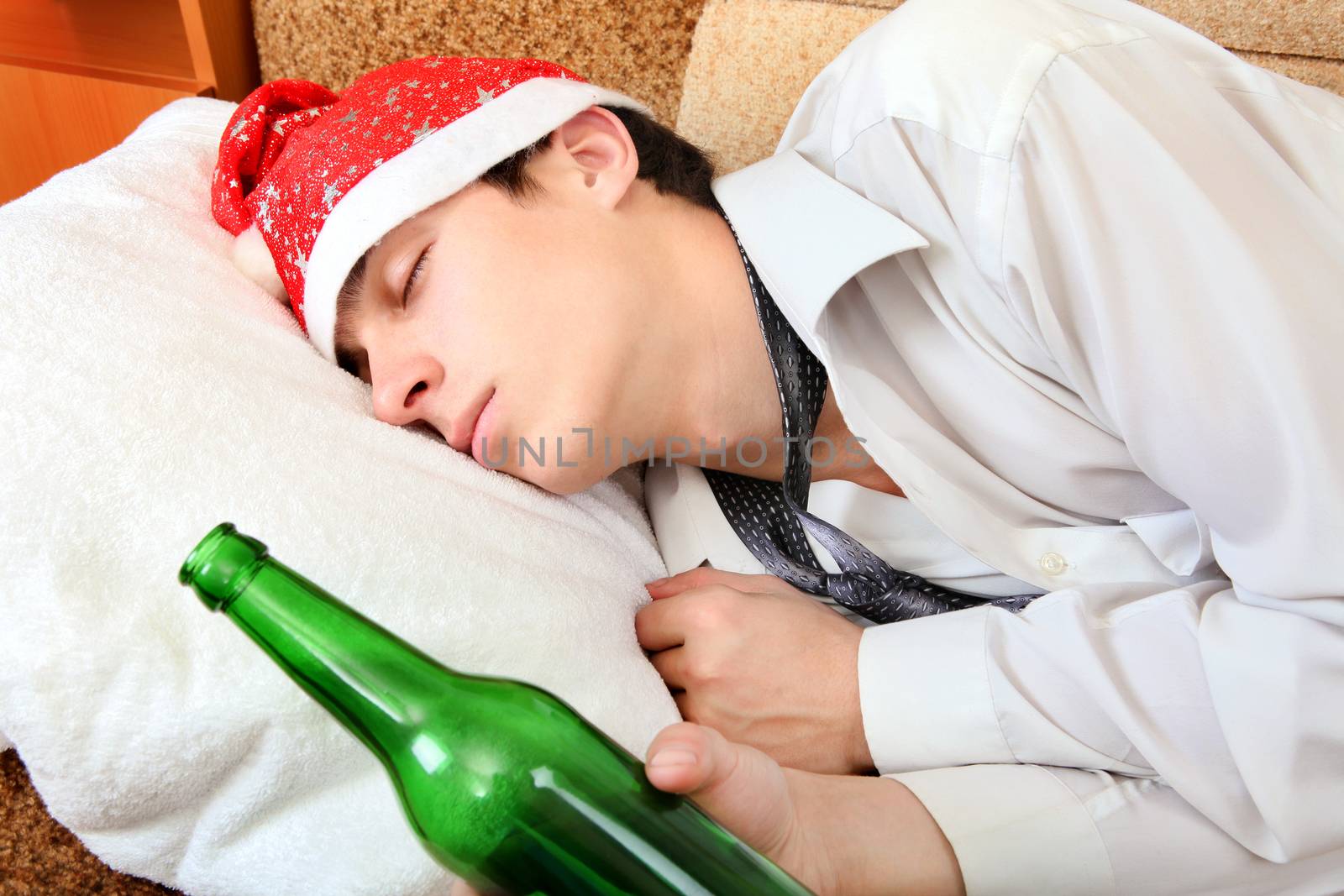 Drunken Teenager sleeping in Santa Hat and Bottle of the Beer on the Sofa