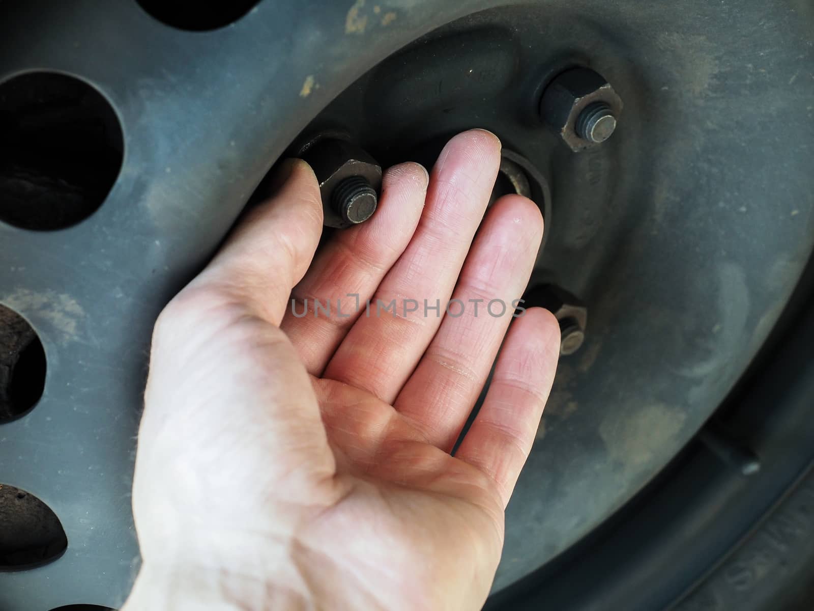 Person Checking Rusty Nuts On A Steel Rim Of A Vehicle with bare hands