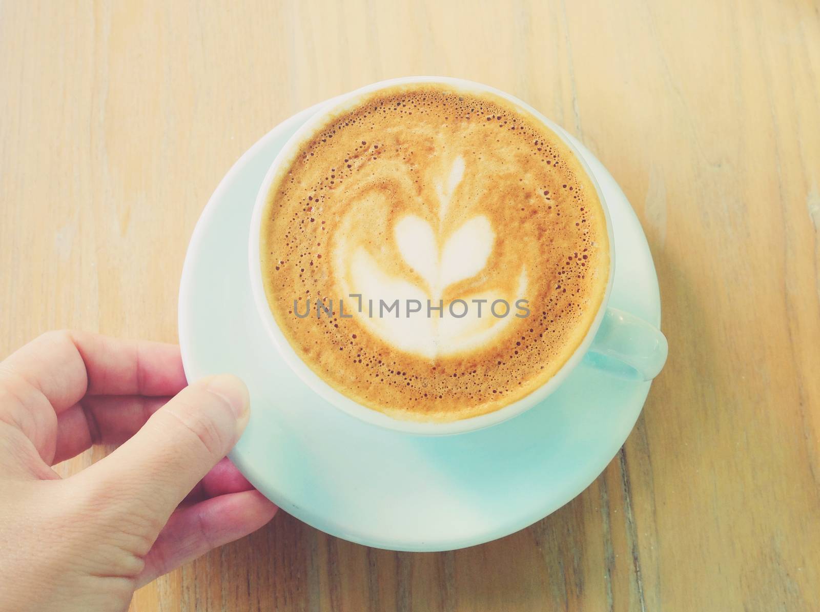 Cup of art latte or cappuccino coffee with hand, retro filter effect