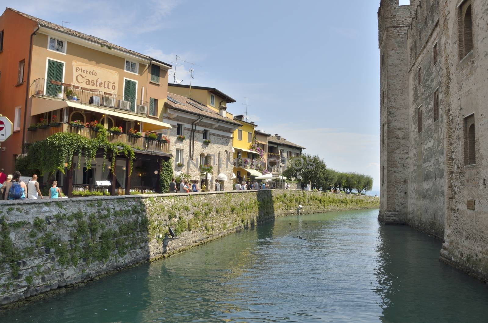 People walking along the road next to the castle by the lake in Sirmione on lake Garda, Italy. 