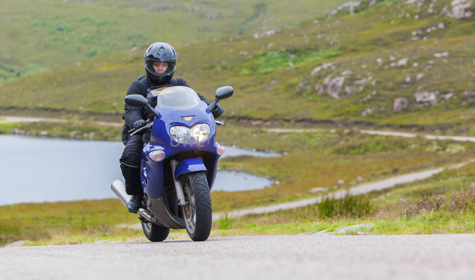 Motorcyclist in the Scottish Highlands, narrow road in mountain landscape