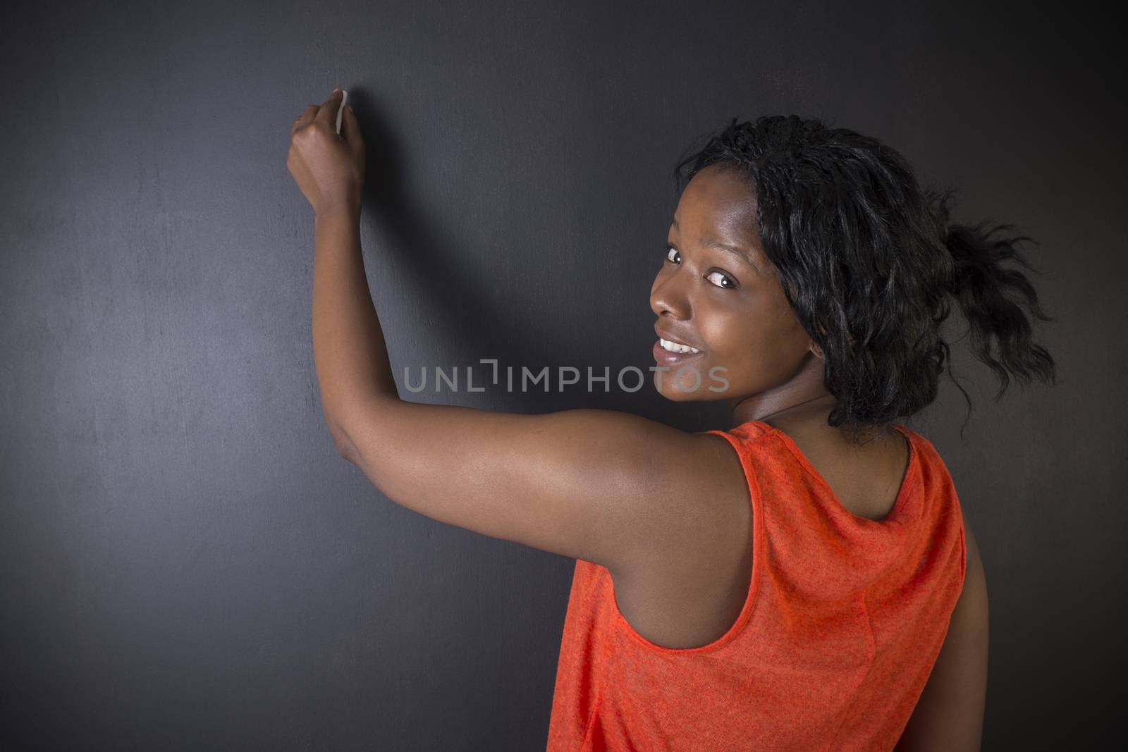South African or African American woman teacher or student writing on chalk black board background