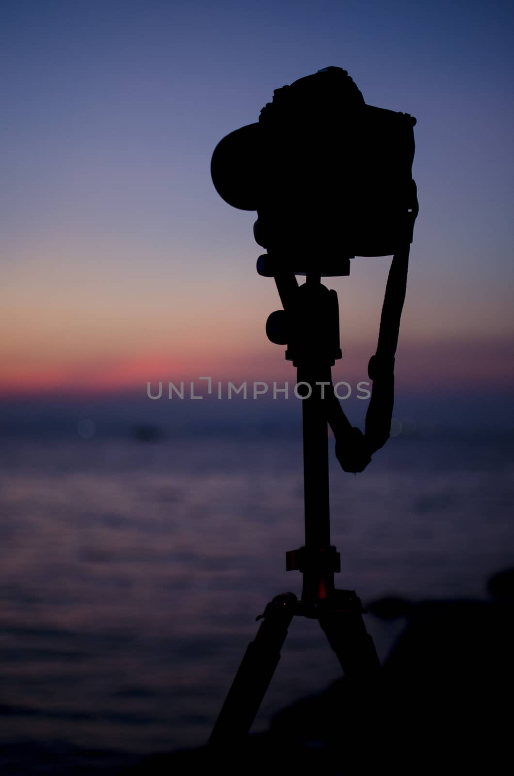 Silhouette of digital camera on tripod with sunset sky at sea blured background