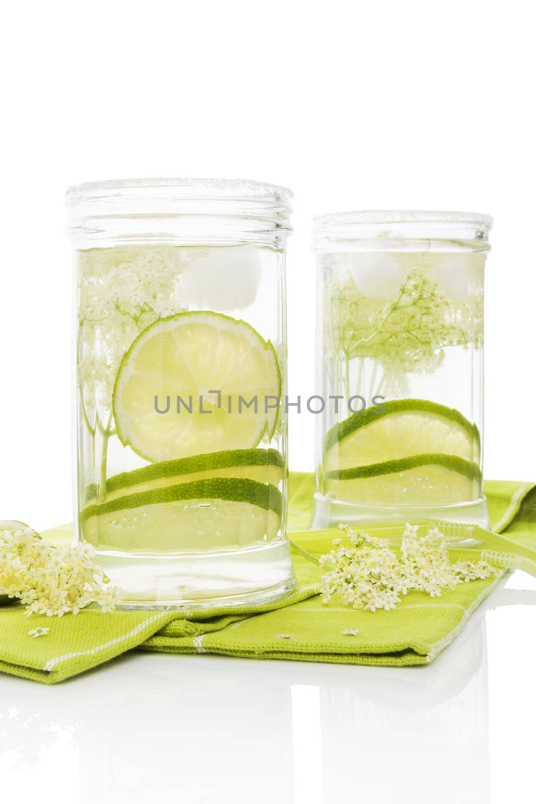 Organic elderberry lemonade with lime slices and ice. Two glasses on green table cloth on white background. Healthy summer drink