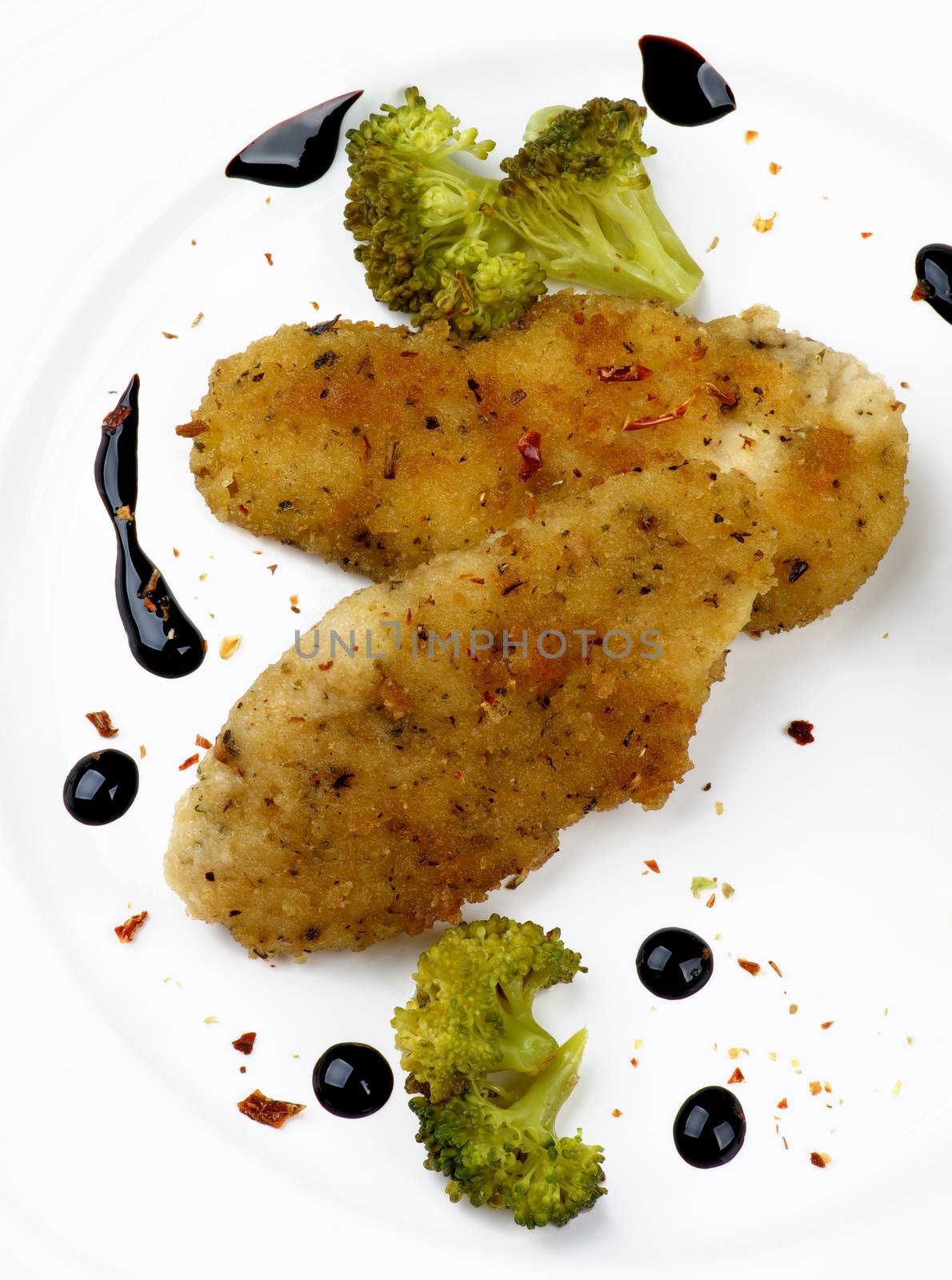 Delicious Fried Chicken Strips in Herb Breading Served with Steamed Broccoli and Balsamic Sauce closeup on White Plate