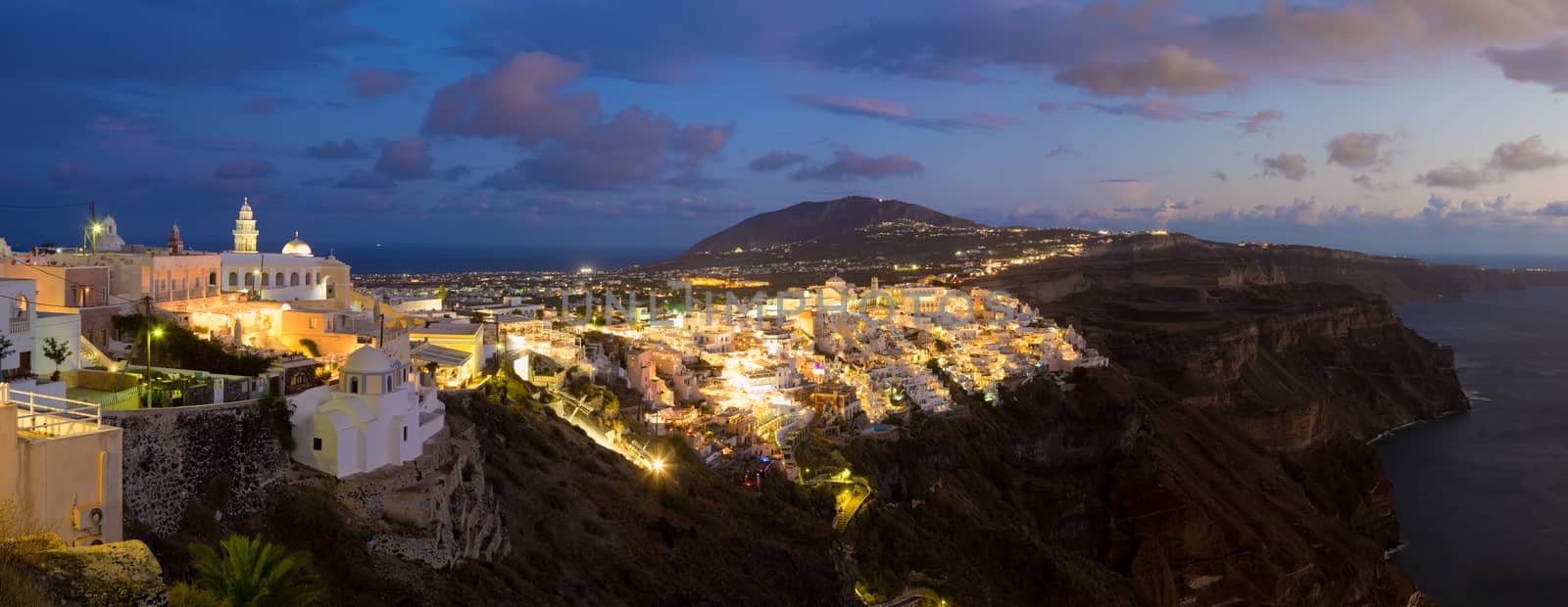 Cityscape of Fira, dramatically located on the edge of the caldera cliff on the island of Thira known as Santorini, Greece. Panorama shot at dusk.