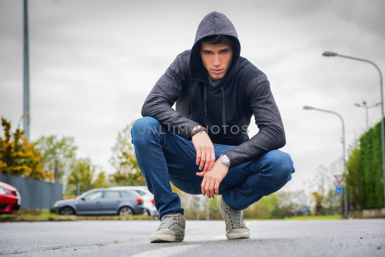 Attractive young man with hoodie and baseball cap in city street by artofphoto