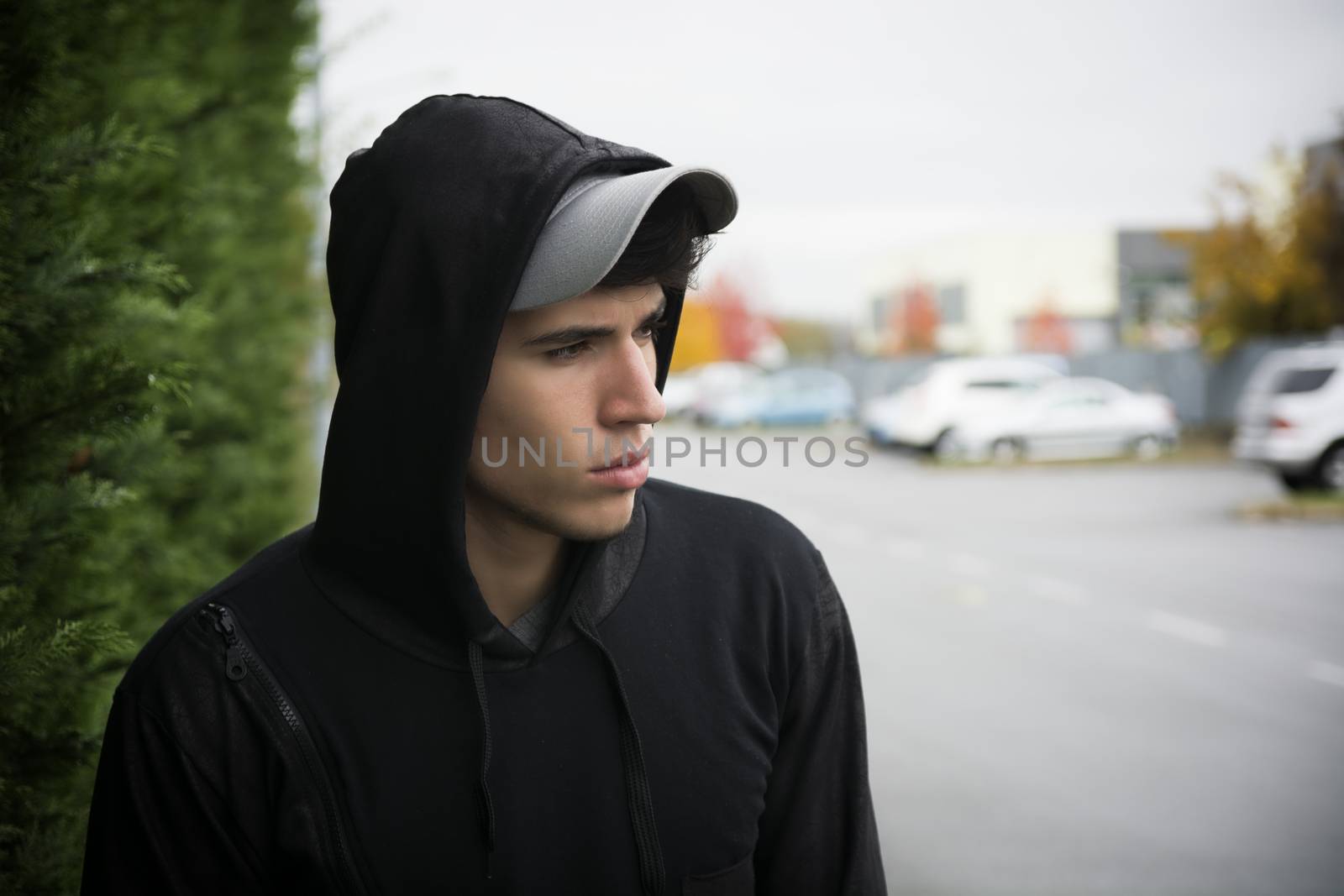 Attractive young man with hoodie and baseball cap in city street, sad or thinking