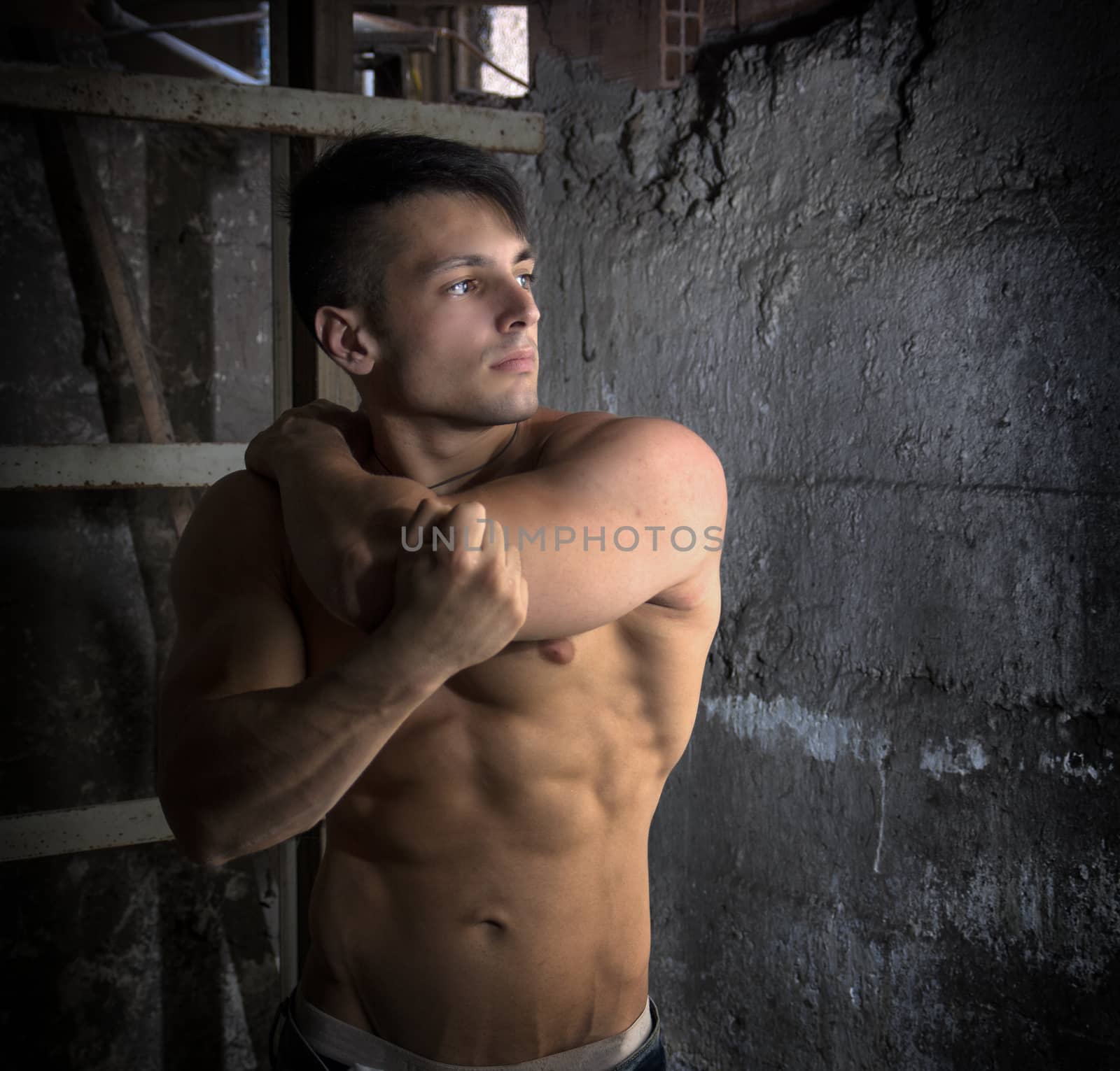 Handsome muscular shirtless young man inside abandoned building near grungy concrete wall