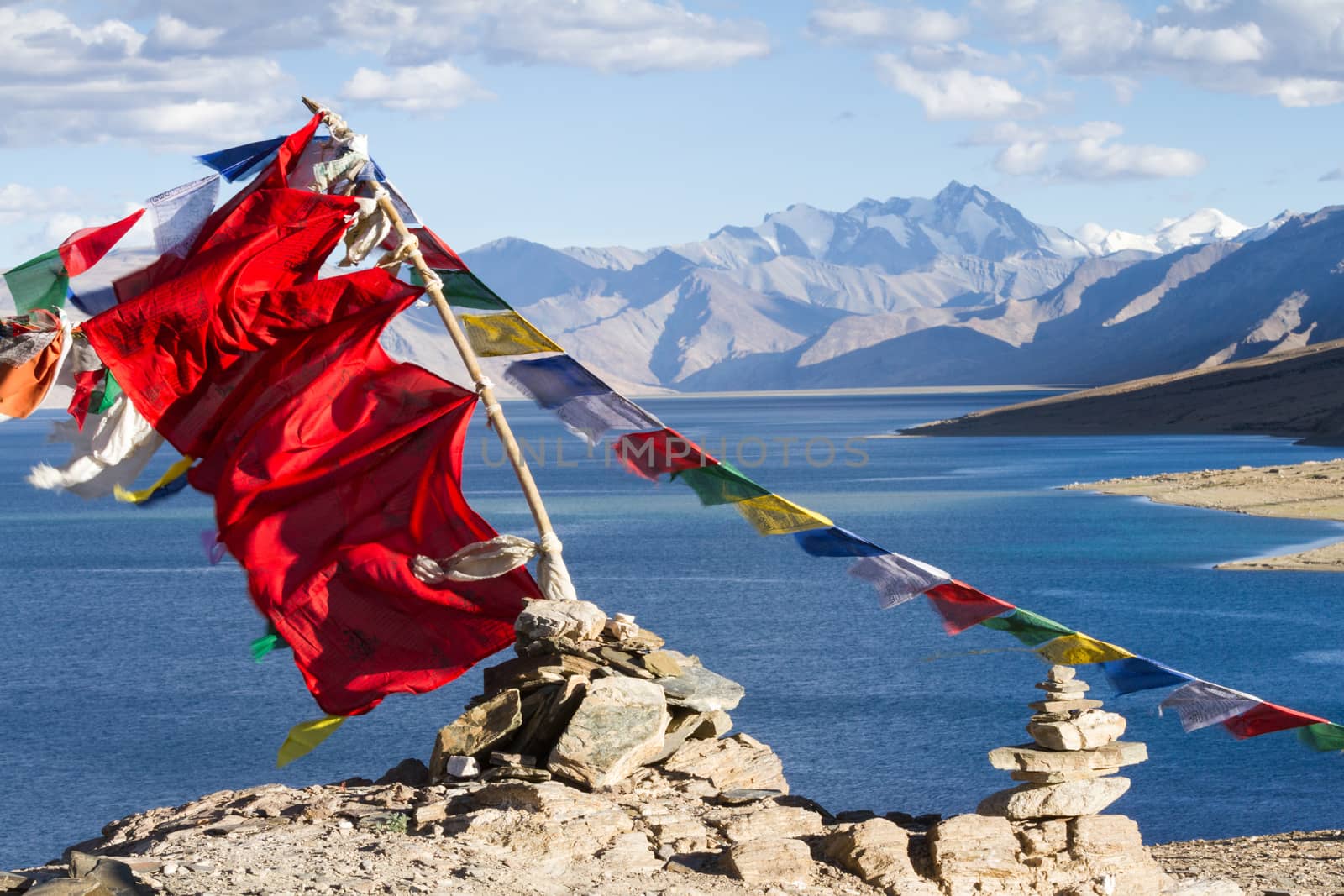 Buddhist prayer flags on the wind against the blue lake, mountains and sky (Ladakh, India)