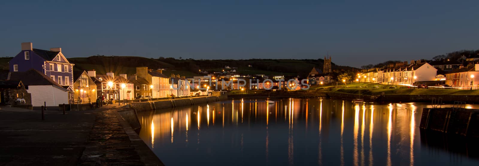 Quaint building overlooking a harbour at dusk, with lights reflecting on the calm water