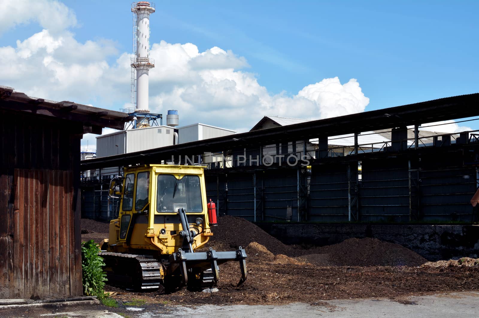 A yellow bulldozer parked infront of a factory.