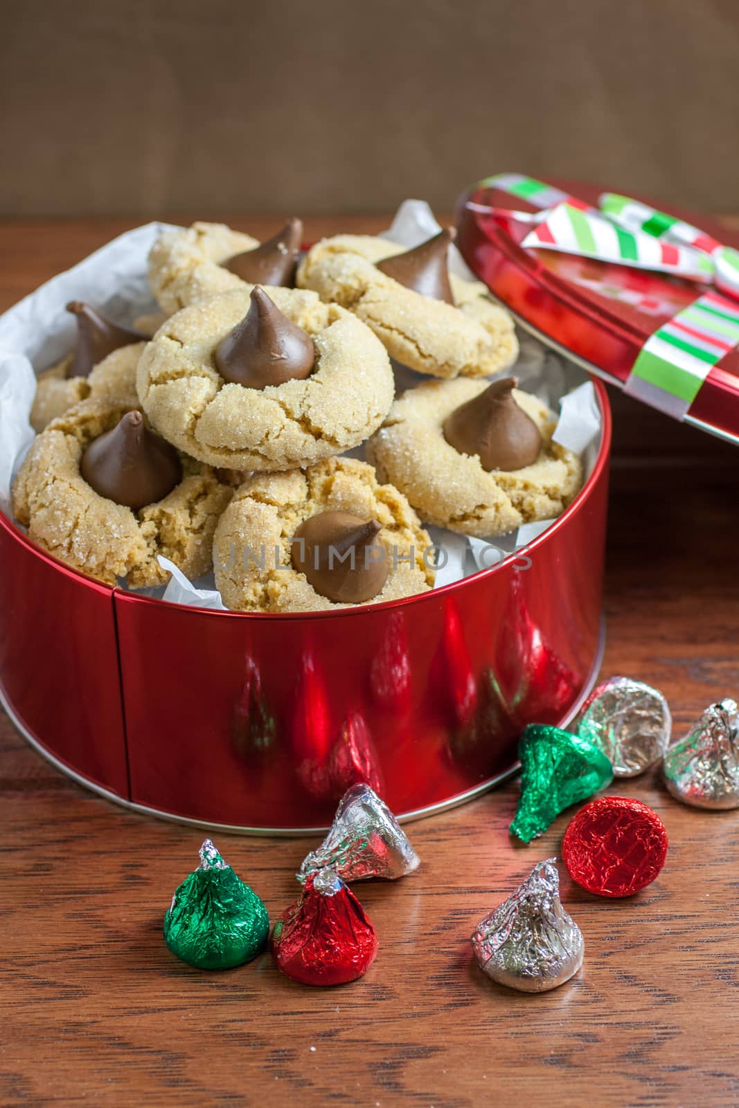 Preanut butter blossoms in a gift tin, highlighted with chocolate candies and and cookies on a wooden table.