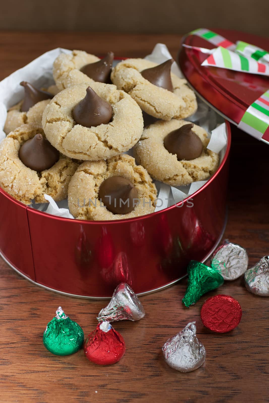 Preanut butter blossoms in a gift tin, highlighted with chocolate candies and and cookies on a wooden table.