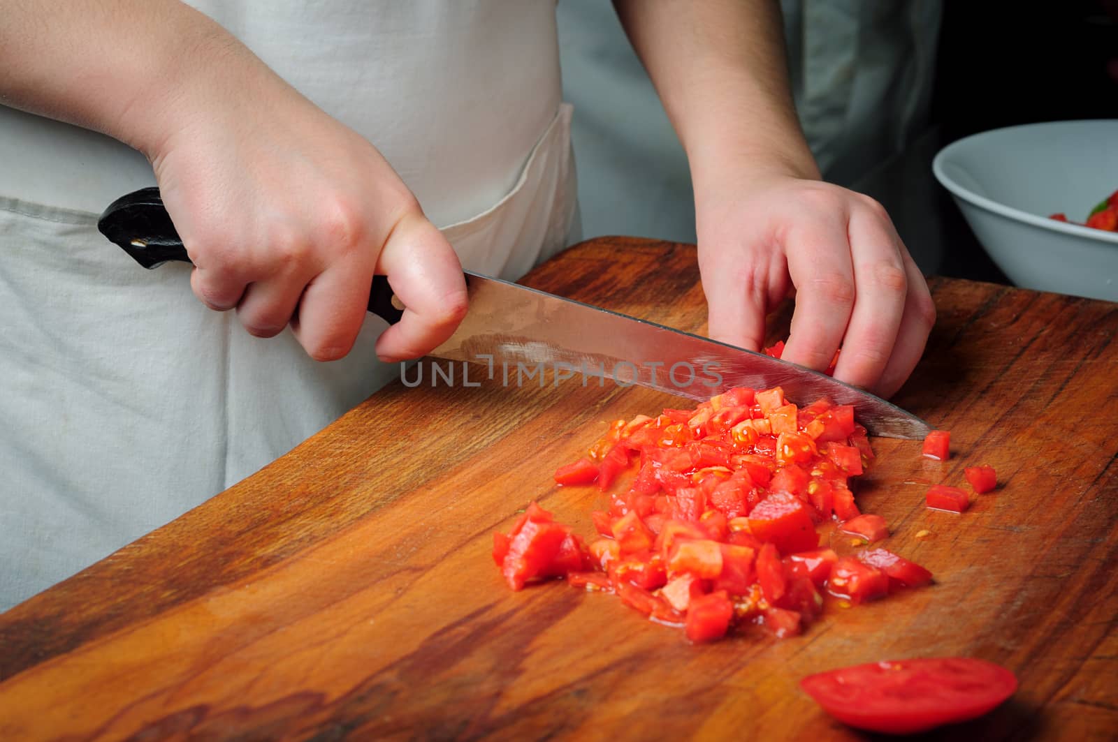 Chief slicing tomatoes on wooden board using knife 