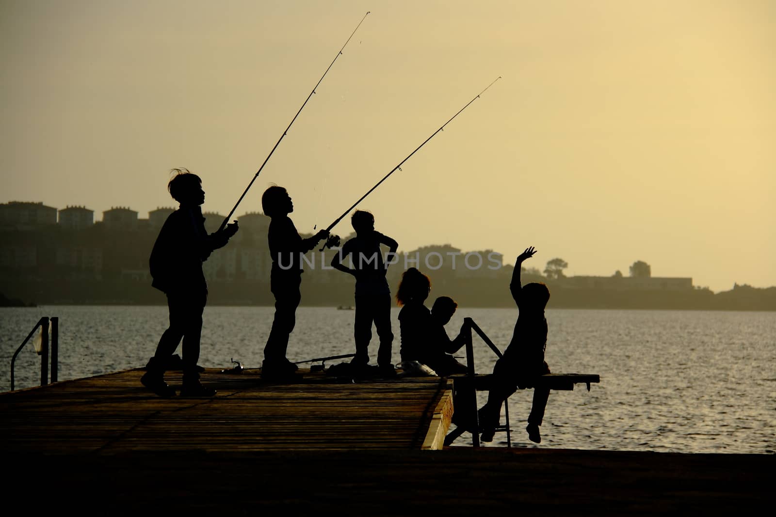 silhouettes of childs on pier catching fish by mturhanlar