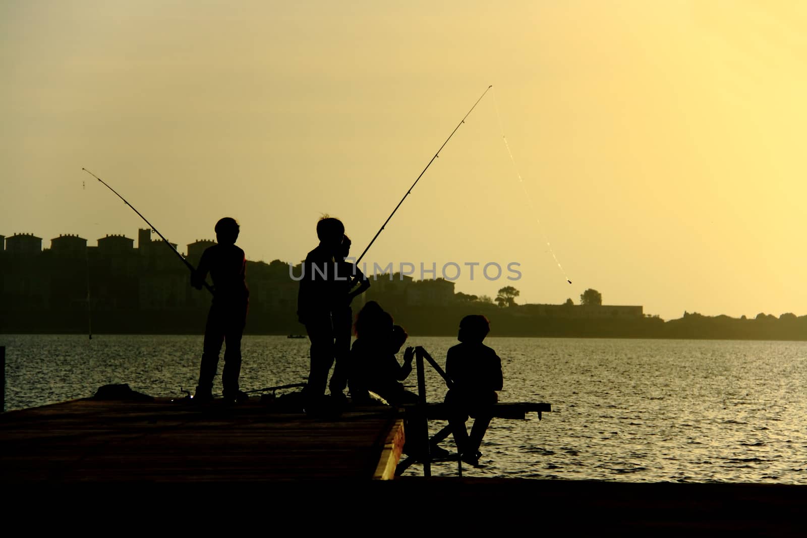 silhouettes of childs having fun ad catching fish on pier at summer evening