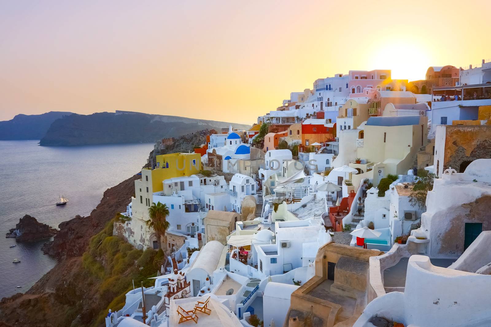 World famous traditional whitewashed chuches and houses of Oia village on Santorini island, Greece. Sunset.