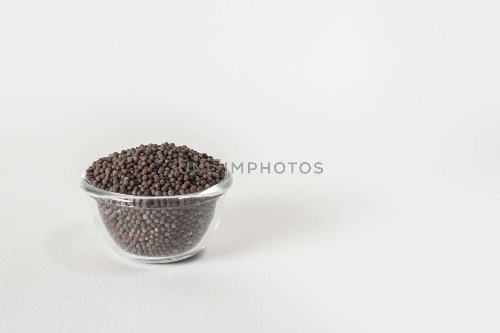 Dry black mustard seeds in a transparent glass bowl on white