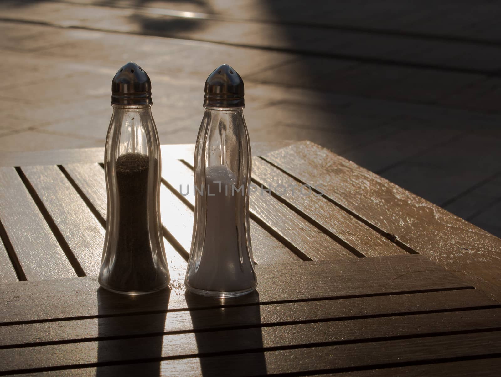 With the last sun rays of the evening, salt and pepper project their shadows on the wooden table