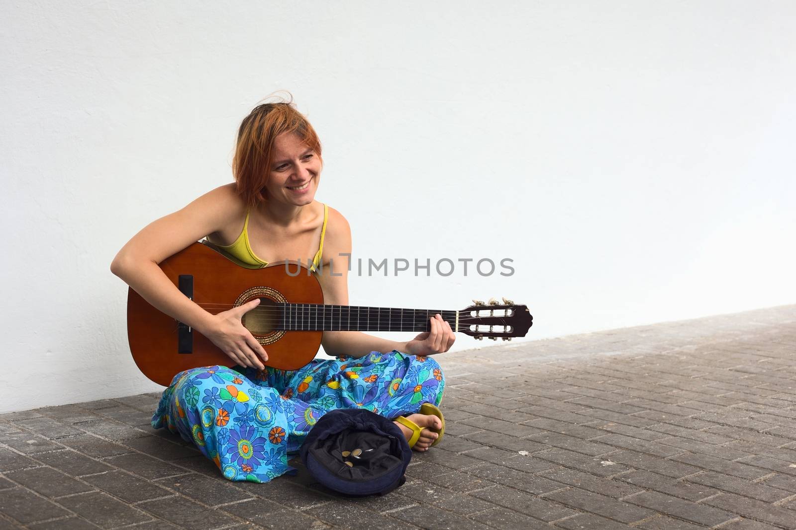 Young woman playing the guitar on the street with a hat containing some coins in front of her 