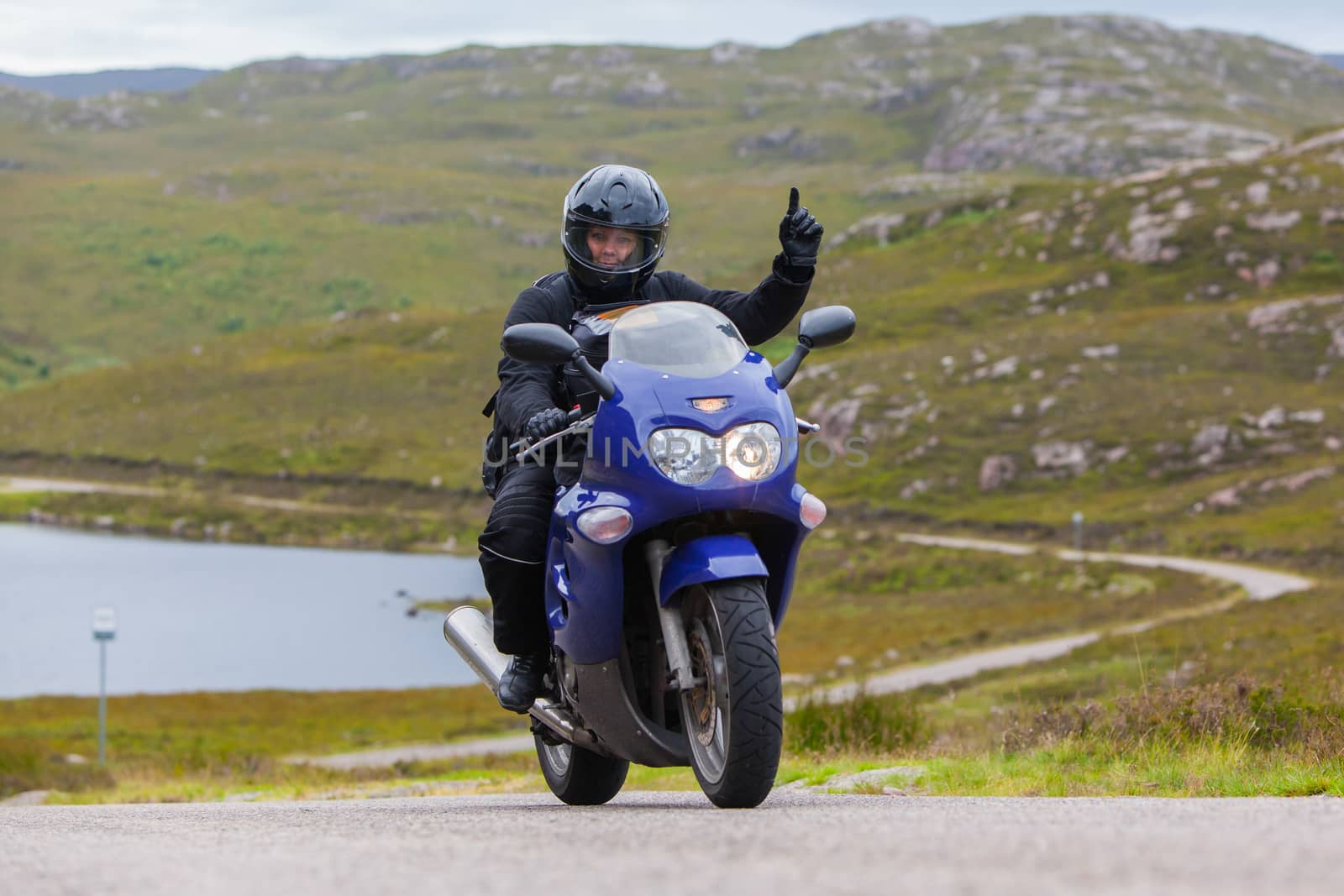 Motorcyclist in the Scottish Highlands, narrow road in mountain landscape