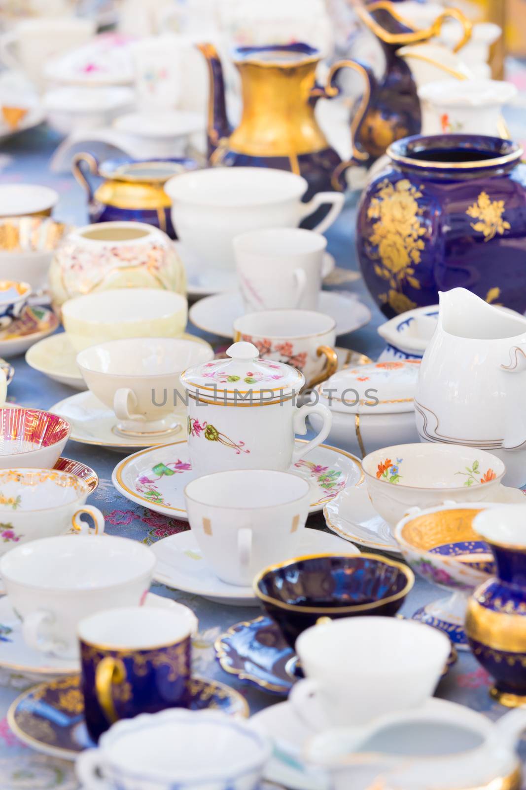 Market boot with sets of vintage china cups beeing selled at the weekend flea market in the city center. Curious visitors in the background.