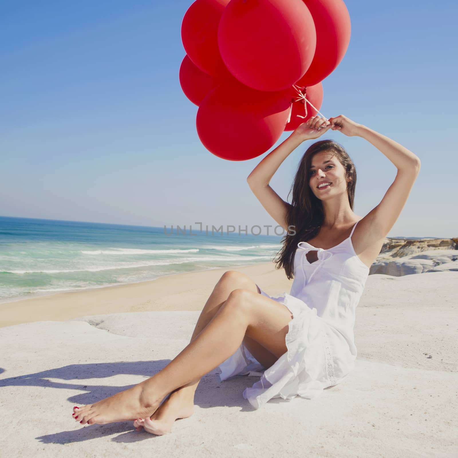 Beautiful girl with red ballons sitting in the beach 