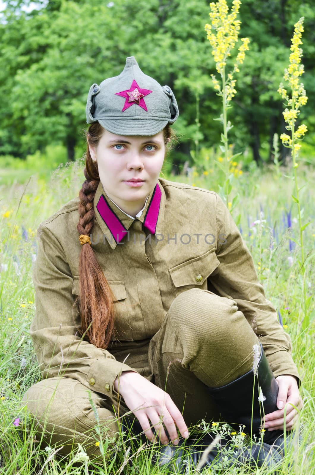 Girl in a red army uniform, sitting on the edge of the forest. Her long braid and blue eyes. Photo taken in the reconstruction of the events of the Second world war