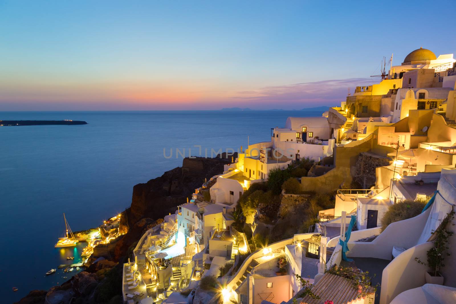 World famous traditional whitewashed chuches and houses of Oia village on Santorini island, Greece. Sunset.