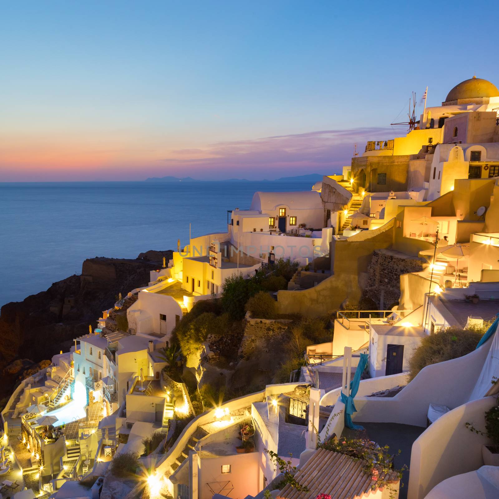 World famous traditional whitewashed chuches and houses of Oia village on Santorini island, Greece. Sunset.