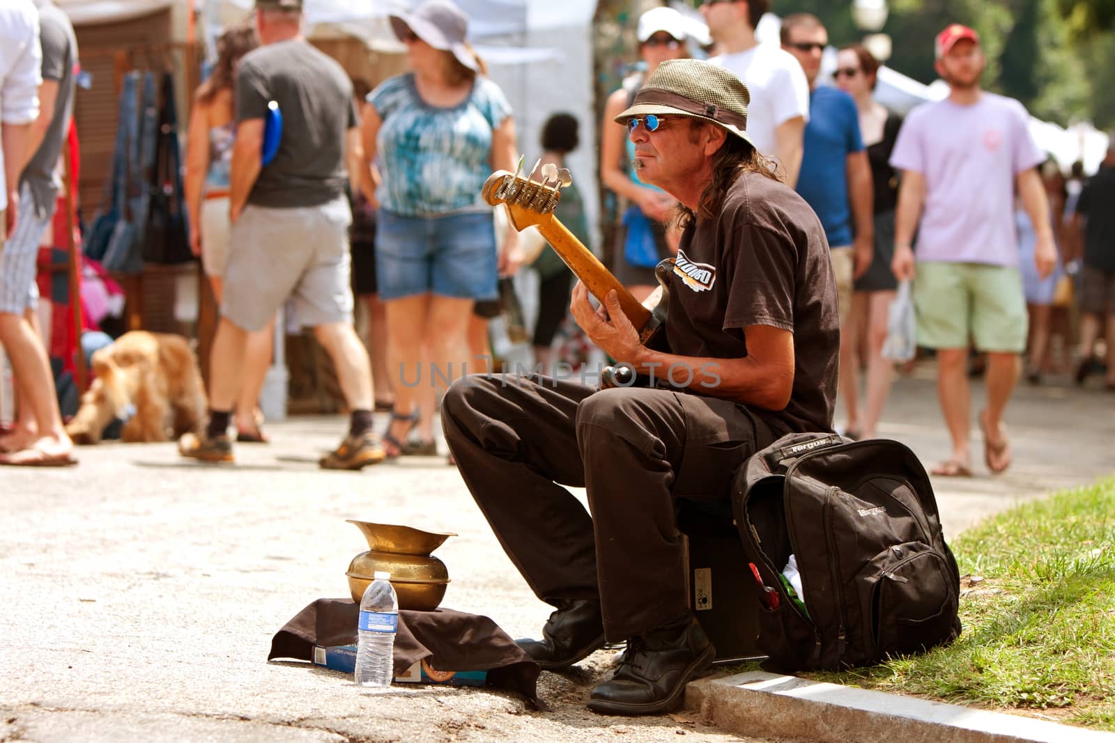Atlanta, GA, USA - August 16, 2014:  A man plays bass guitar for tips while sitting on the curb at the Piedmont Park Arts Festival.  