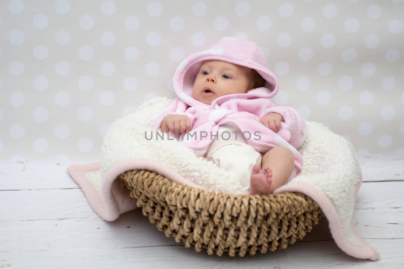 baby girl in a pink bathrobe sitting in a basket