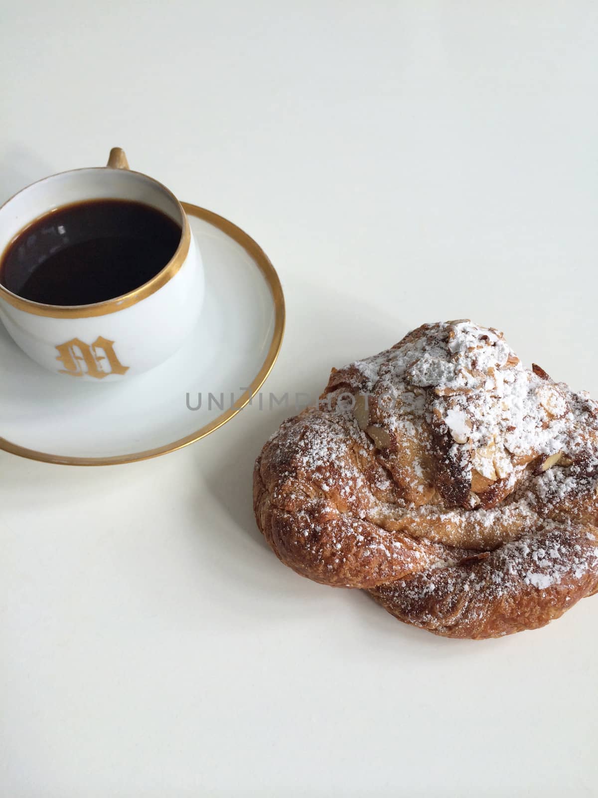 Amond croissant and black coffee in a white and gold mug with the letter M