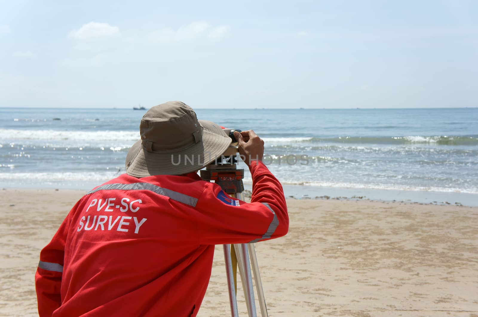 BINH THUAN, VIET NAM- OCT 21: Asian engineer work on Vietnamese beach, man looking in theodolite to survey sea level, measurement device set on tripod, Vietnam, Oct 21, 2013