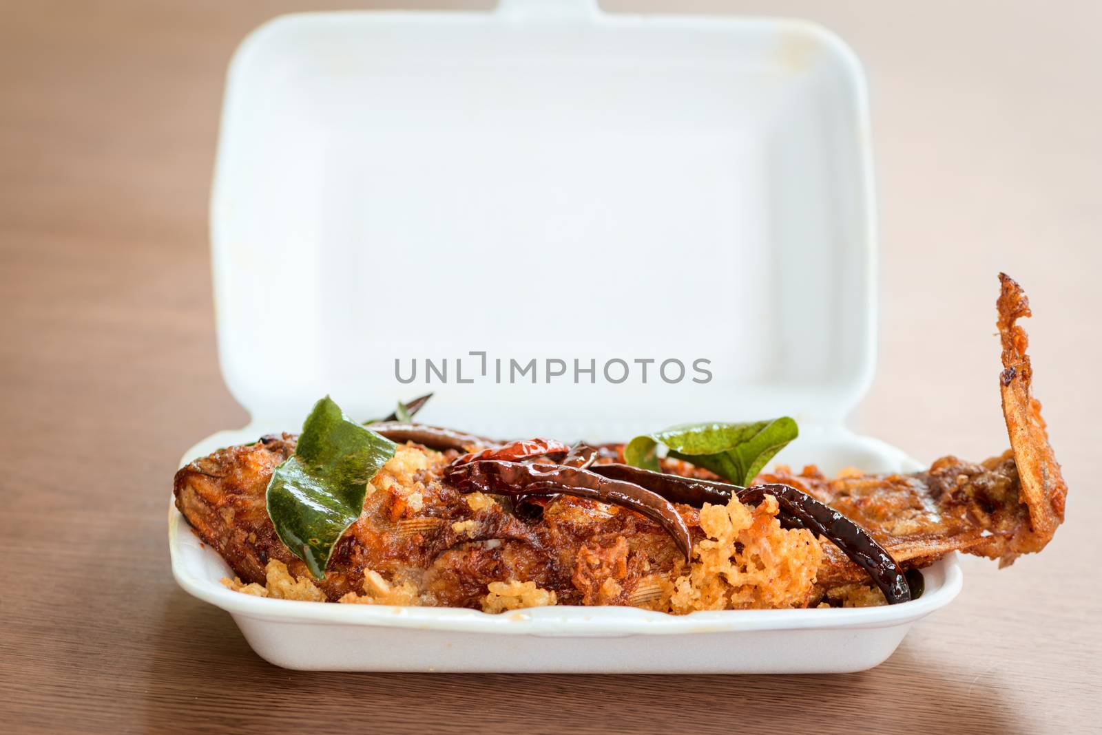 Sour fried full cooked fish with spicy hot red chili pepper in white take away bowl on wooden table