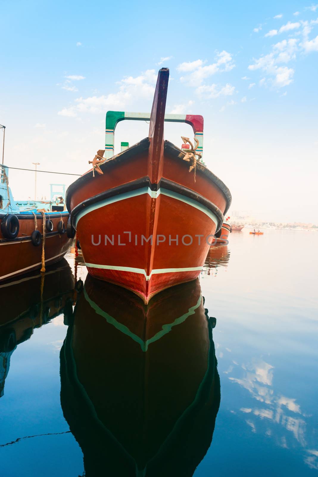Big wooden cargo boat with reflection in blue water moored up in a port