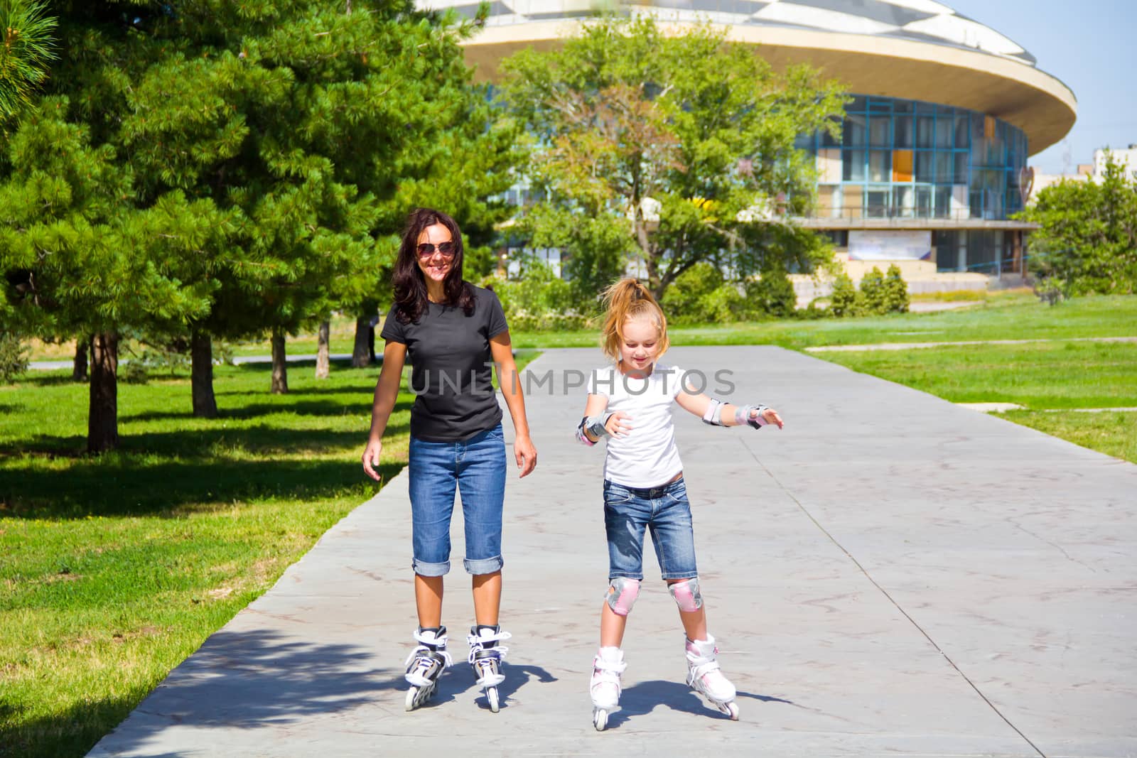 Learning mother and daughter on roller skates in summer