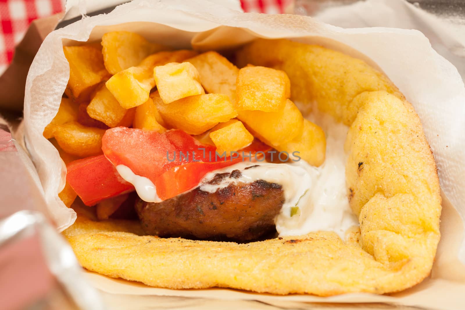 View of a Greek traditional soutzoukaki wrapped with pitta from corn, which contains fried fries, yoghurt, onion and tomato