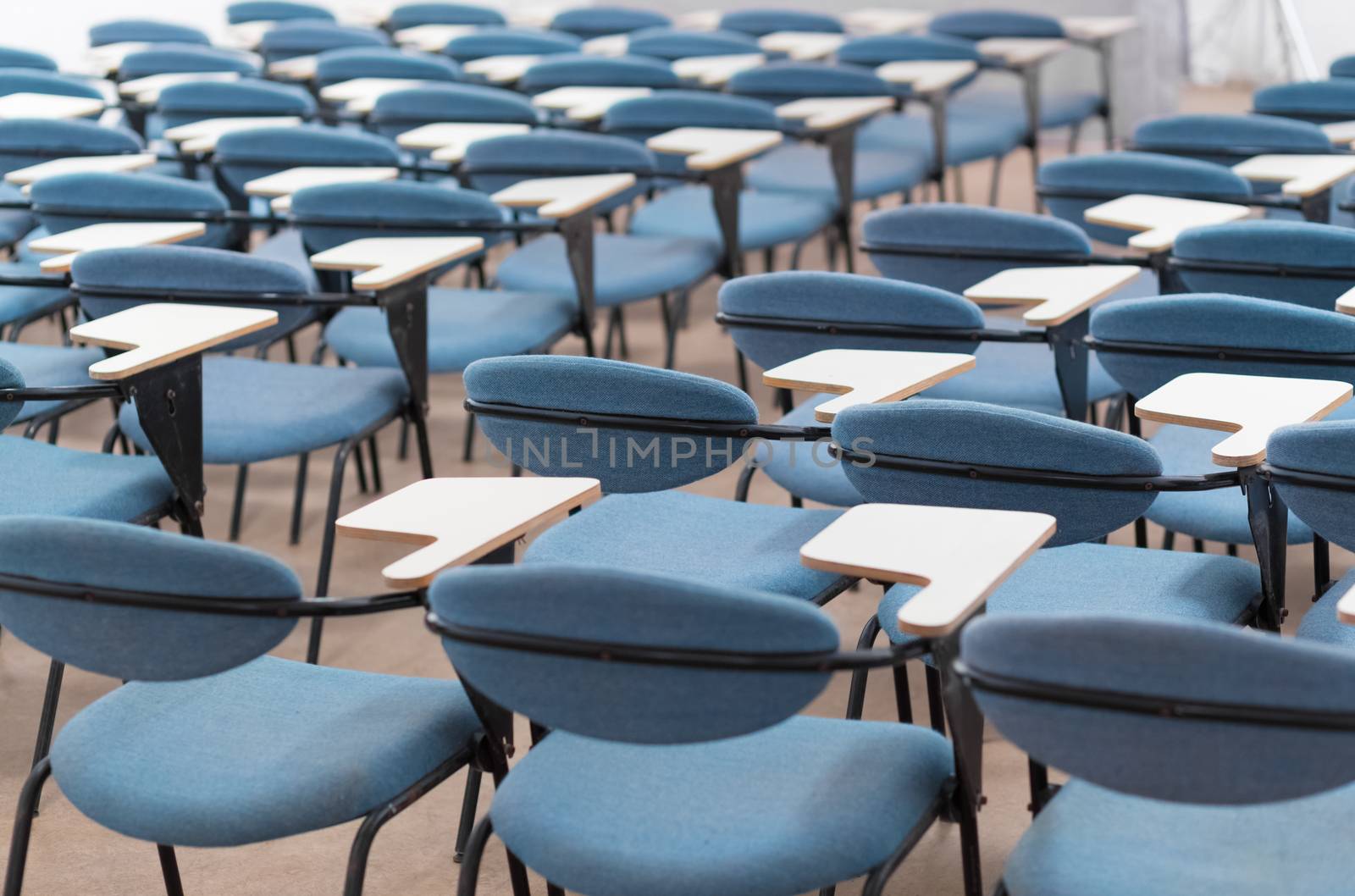 Interior of empty conference hall with blue velvet chairs with small desks for writing notes.