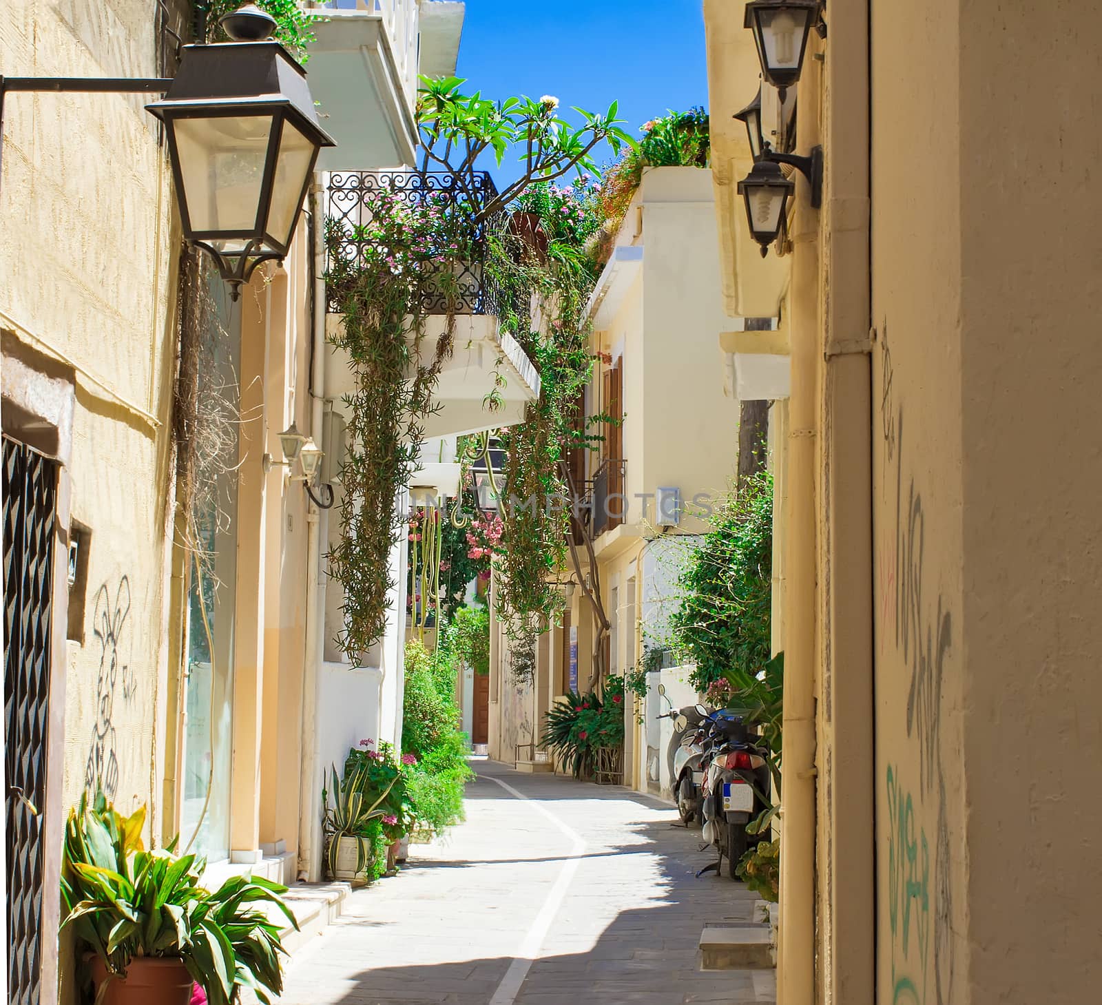 Narrow street with old buildings and a balcony with flowering plants in the old part of the city Retno, Crete, Greece.