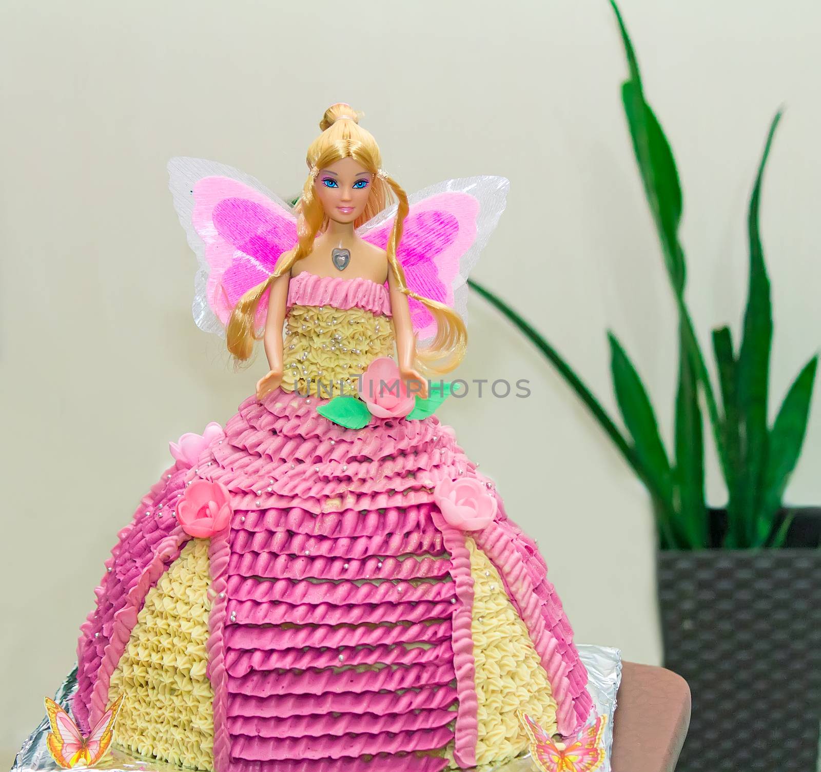 Beautiful birthday cake in the form of a doll in a wide dress, made of sponge cake and decorated with pink and yellow cream.