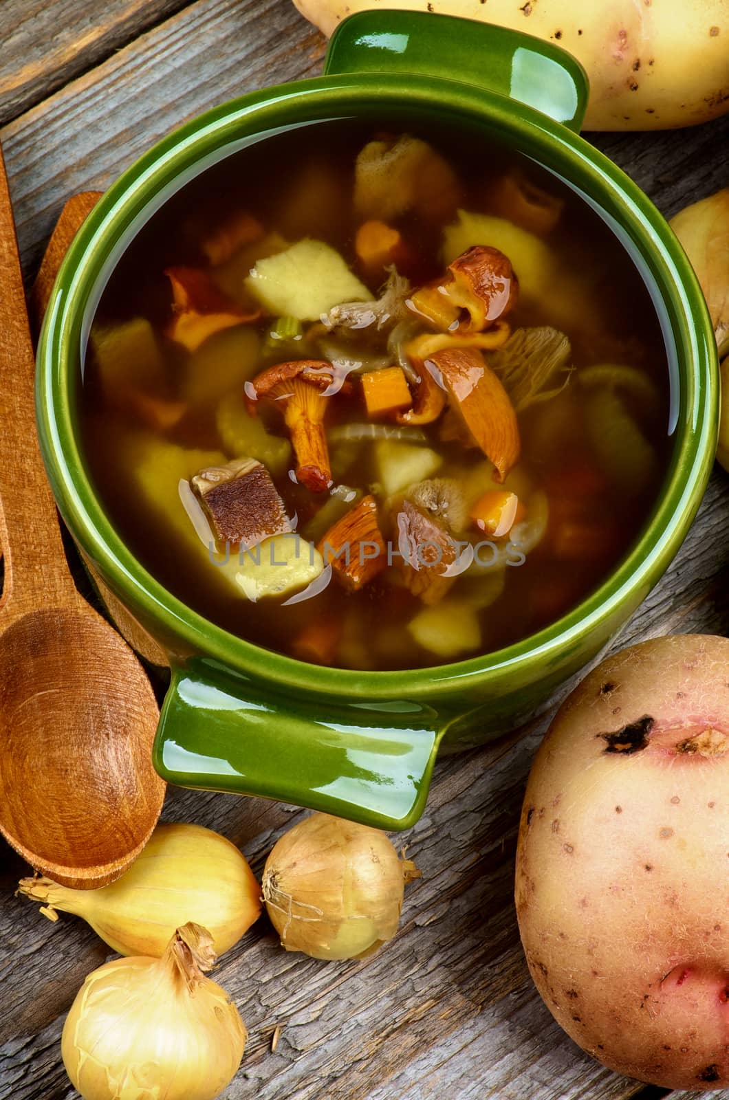 Delicious Vegetarian Soup with Chanterelle Mushrooms  in Green Pot with Raw Potato, Onions and Wooden Spoon closeup Rustic Wooden background. Top View